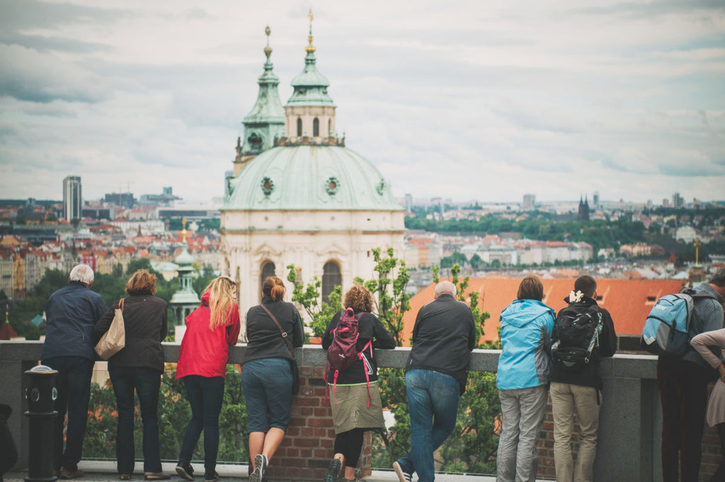 a group of tourists with a tour guide enjoying a spectacular view of St. Nicolas Church from one of the royal gardens of the Prague Castle