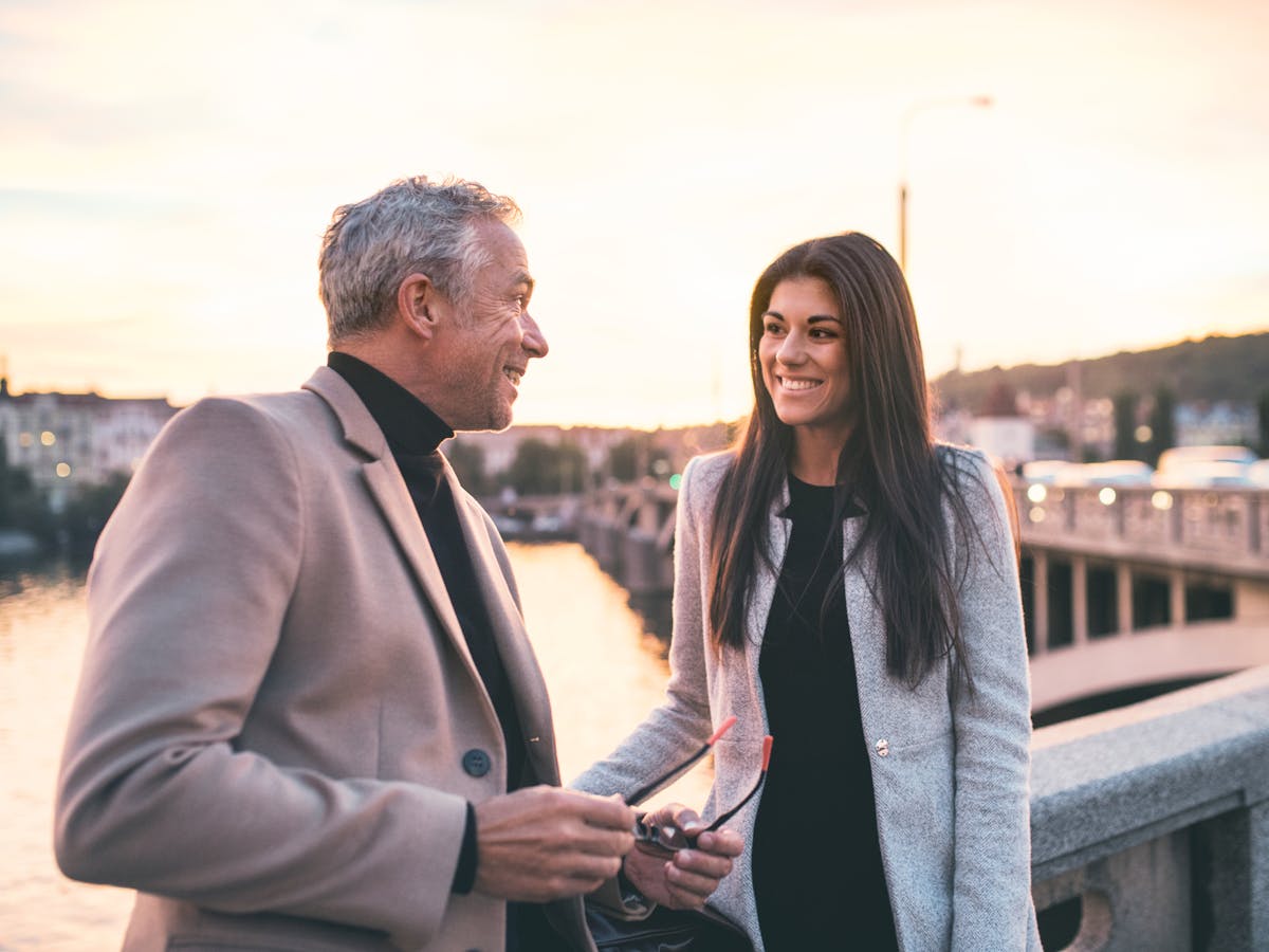two people in suits standing on the banks of Vltava River smiling at each other