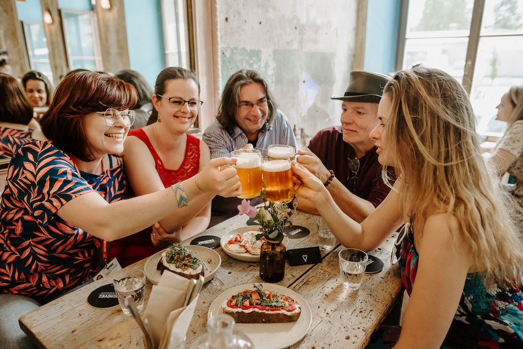 a group of tourists sitting in a bar in Prague, raising their beer glasses to cheer