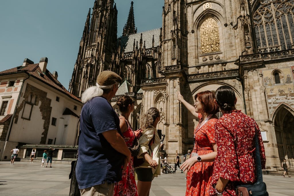 a tour guide pointing to the gothic architecture of the St. Vitus Cathedral in front of a group of tourists on the Prague Castle tour