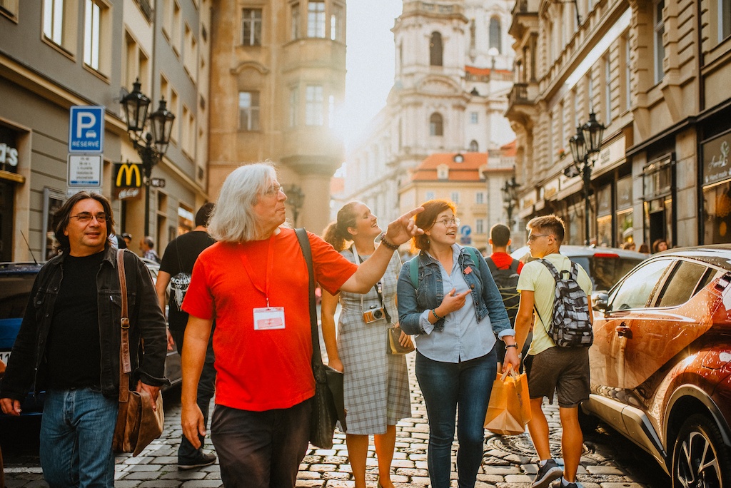 a group of tourist walking on a city street in Prague together with a local tour guide pointing out the beauties of autumn in the city