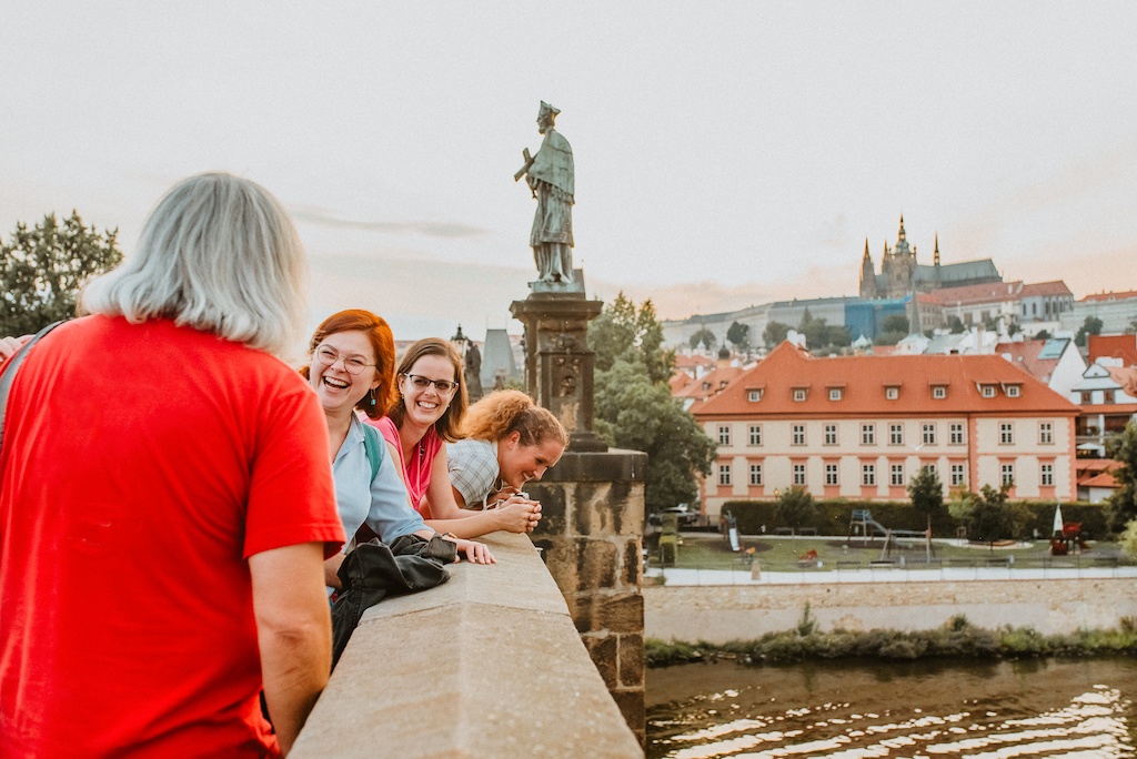 a group of tourists facing a tour guide on the Charles Bridge with a view of Prague Castle in the background