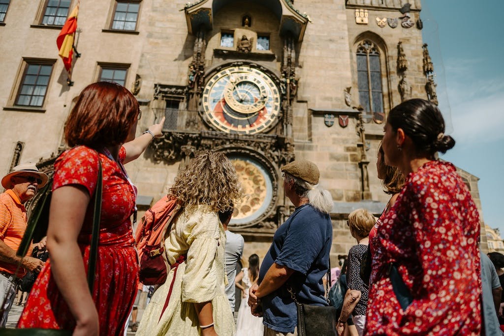 a tour guide standing in front of a group of tourists, pointing at the Prague Astronomical clock