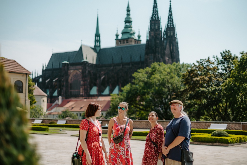 a group of tourists and a tour guide in one of the royal gardens of Prague Castle with a view of St. Vitus Cathedral in the background