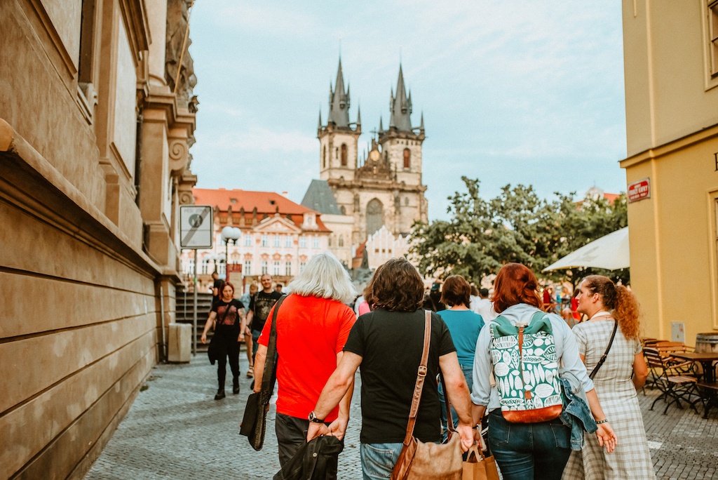 a group of tourists following a tour guide into the Old Town Square in Prague with a view of the Tyn Church in the background