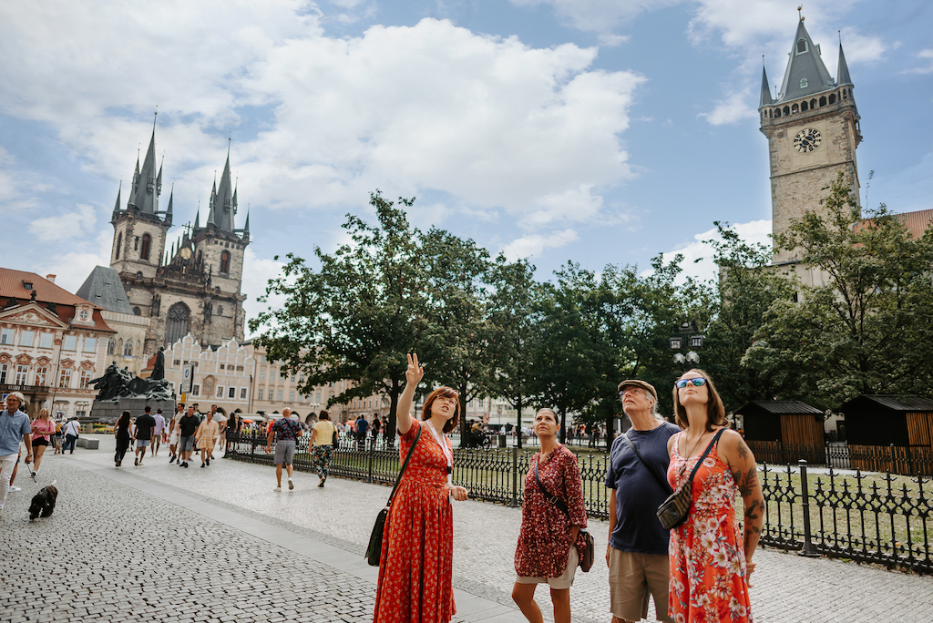 a tour guide from Prague City Adventures showing her guests the historical facades in the Old Town Square in Prague with the beautiful Tyn Church in the background