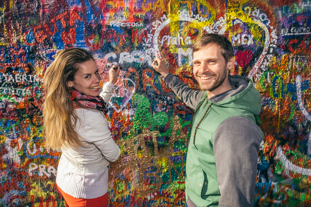 a young couple drawing a heart together on the John Lennon wall in Prague's Kampa Park