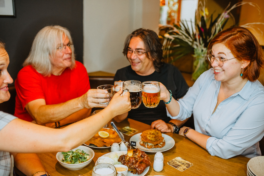 a group of people sitting a table full of traditional Czech dishes with a glass of delicious Czech beer in hand