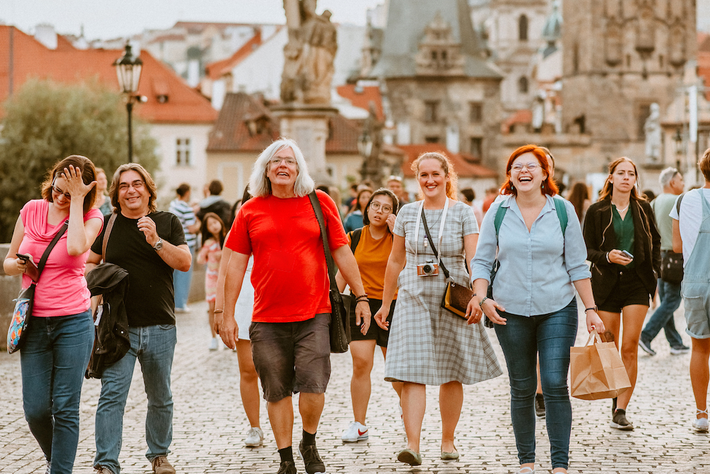 a group of people following a tour guide across the Charles Bridge in Prague