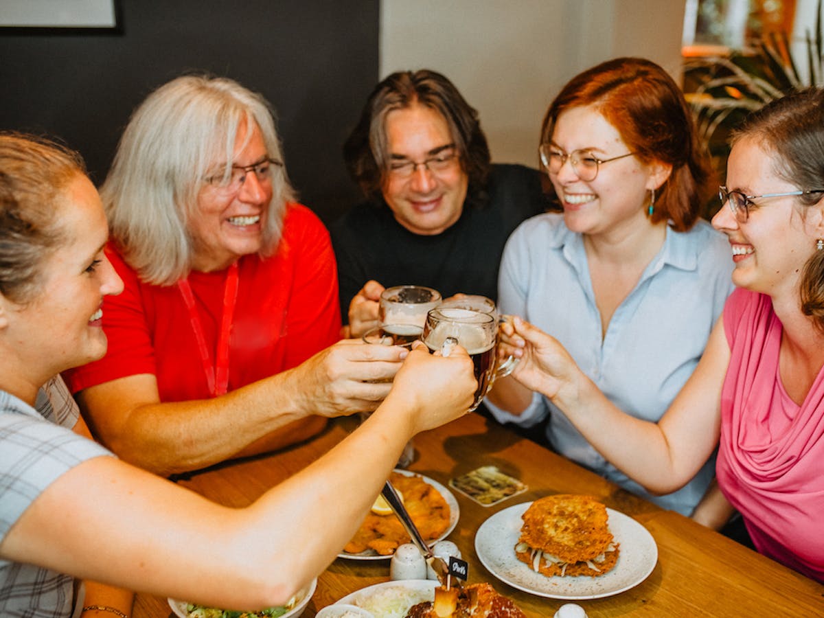a group of people sitting at a table eating delicious-looking traditional Czech food and raising their beer glasses for a toast in a local restaurant in Prague