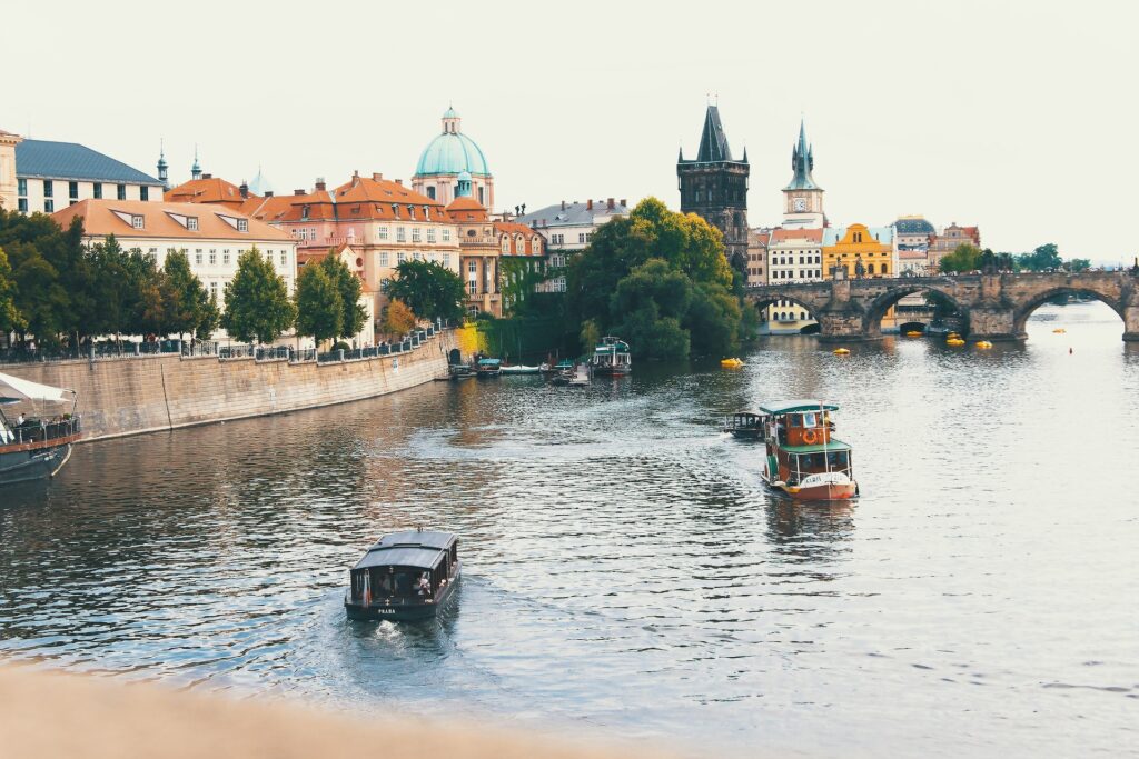 two small boats on the Vltava River in Prague with a view of the Charles Bridge in the background