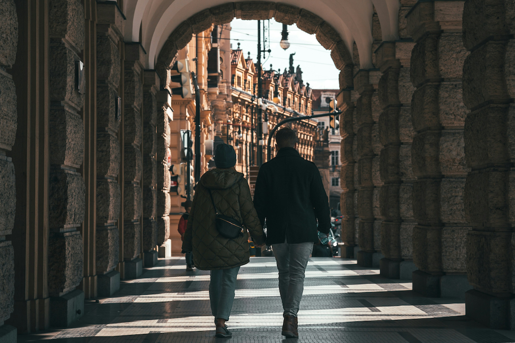 a couple holding hands walking in front of the building of the Charles University in Prague