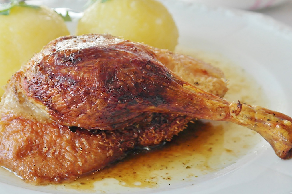 a close up of a roasted duck leg and potato dumplings in the background