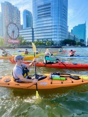 a group of people riding kayaks in the water with the Colgate Clock in the background