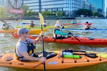 a group of people riding kayaks in the water with the Colgate Clock in the background