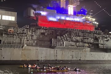 kayakers in front of the Intrepid Aircraft Carrier at night