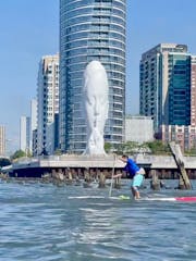 a man on a stand up paddle board in front of a sculpture of a woman's face