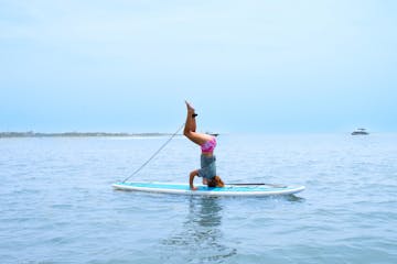 a girl doing a headstand on a paddleboard