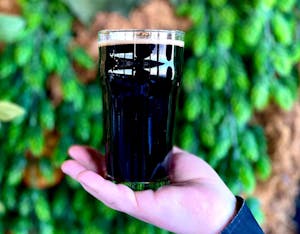 Close up of a Maine Stout in a glass held out by woman's hand 