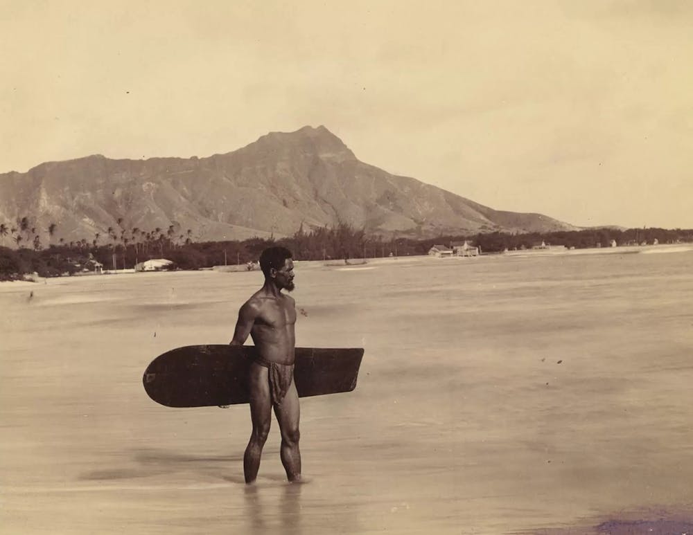 a person holding a surf board in front of a mountain