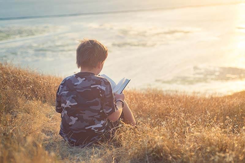 A boy reading outside during sunset for International Children's Book Day