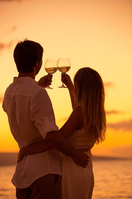 A couple toasting Champagne in front of a sunset near the ocean for a marriage proposal or a wedding at sea