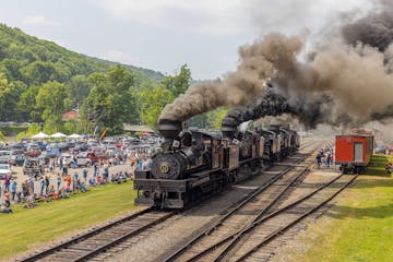 a steam train on a track with smoke coming out of it with Cass Scenic Railroad State Park in the background