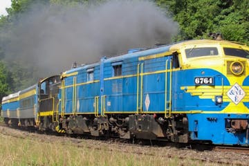 a blue train traveling down train tracks near a forest