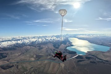 tandem skydiver freefalling with snow covered mountains and a bright blue lake
