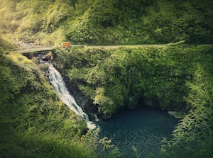 view of Makapipi Falls. waterfall under bridge as orange van drives along road 