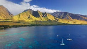 Aerial view of the west coast of Maui with visible coral reef, sailing boats and green mountain on the background. Area of Olowalu, Hawaii