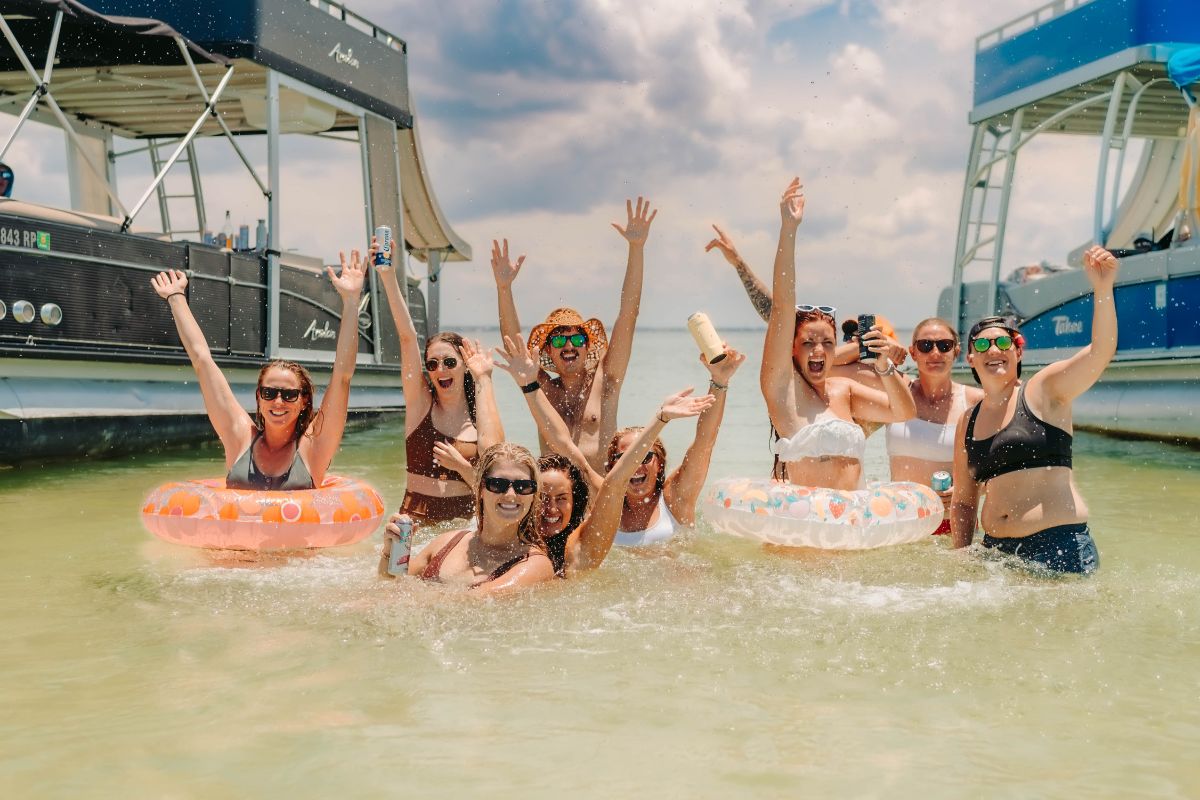 bachelorette group in floaties with bach boats in background