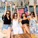 small group raising their arms on a private yacht cruise in NYC with the American flag and skyline in the background