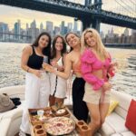 friends standing on a private yacht during a sunset cruise in NYC with the city skyscrapers and bridge in the background