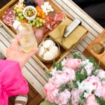 hand with pink ruffles grabbing a champagne flute with charcuterie board and pink flowers makes how much to rent a boat in nyc a priceless event