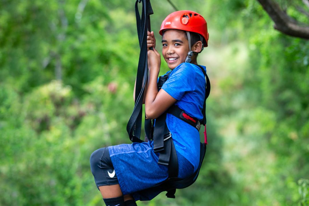 a young boy wearing a helmet ziplining at Coral Crater