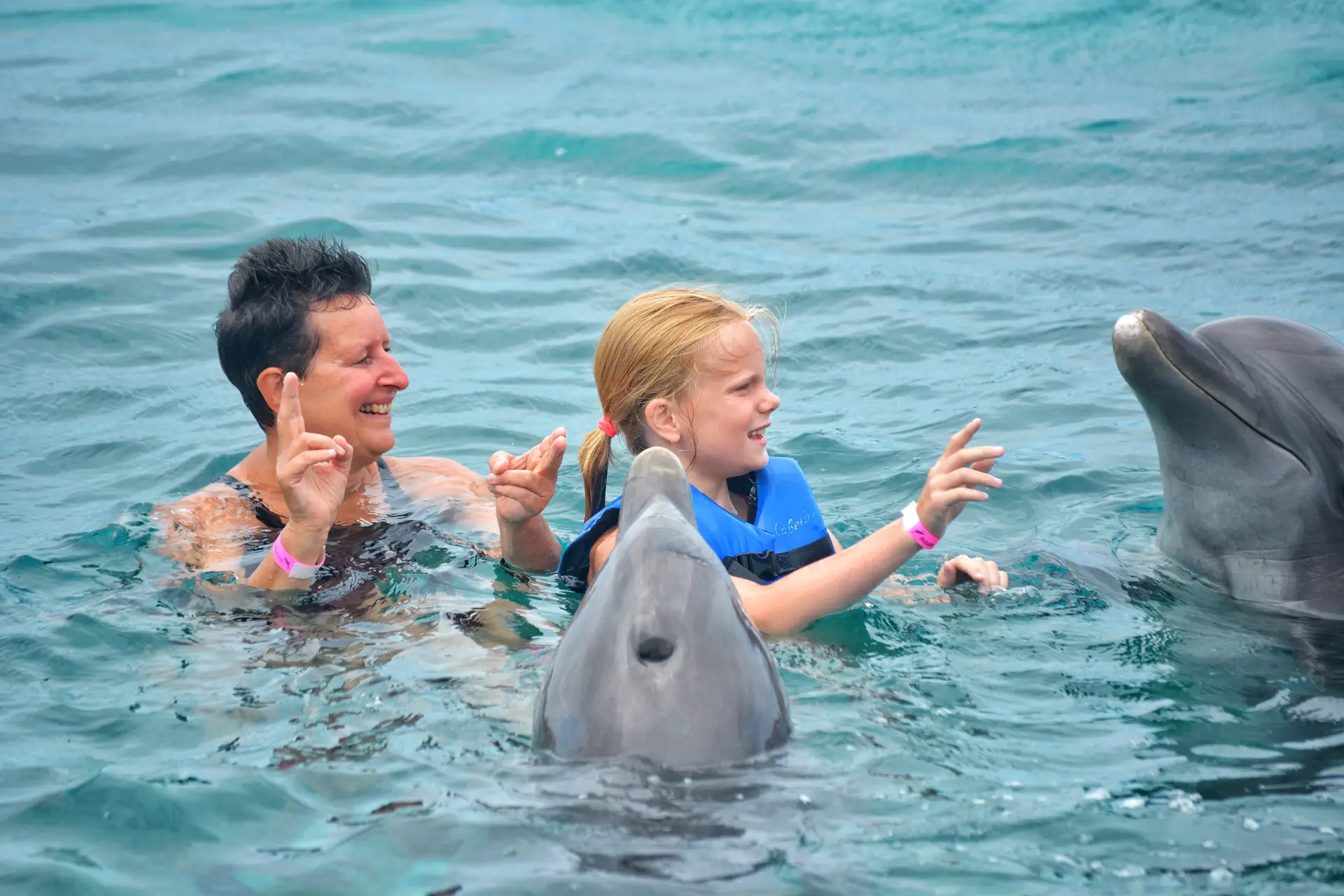 A man guides a young woman in interacting with dolphins.
