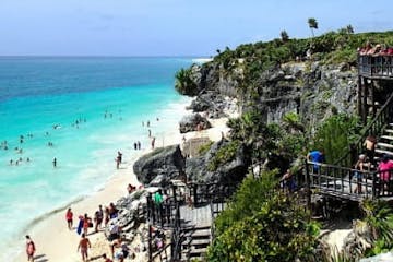 a group of people standing next to a body of water with Tulum in the background