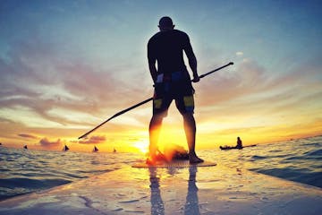 a man standing in front of a sunset on a paddleboard