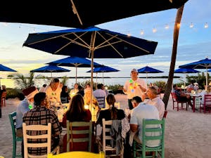 a group of people sitting at a beach umbrella eating and appreciating a florida keys sunset