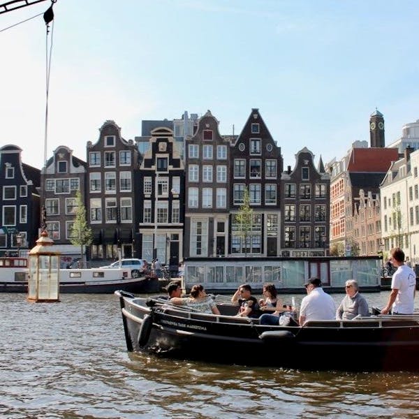 a group of people in a small open boat cruising down an amsterdam canal