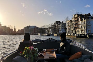 a couple sitting on an open boat tour on amsterdam canal with the sunset in the background