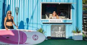 a woman holding a surf board next to a shop's entrance