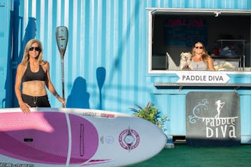 a woman holding a surf board next to a shop's entrance