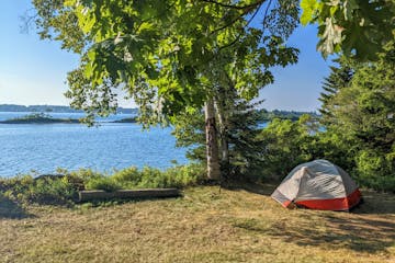 An island campsite with an open area, tent, and trees. Water in the distance.