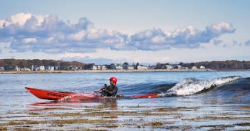 Joe G surfing a sea kayak at a Maine beach