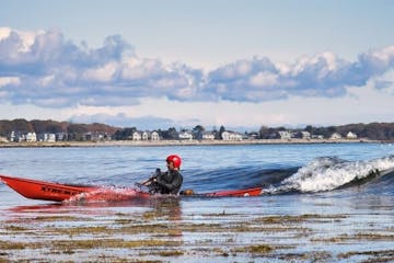 Joe G surfing a sea kayak at a Maine beach