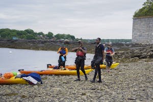 A group of people and their kayaks standing on a cobble and boulder beach