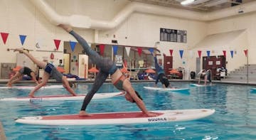 People doing yoga on paddleboards floating in an indoor pool