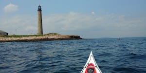 The bow of a kayak in the foreground with Petit Manan Light, a remote lighthouse, in the background